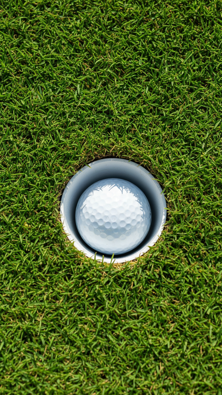 Golf Ball Resting At Bottom Of Pristine Hole On Sunny Putting Green For Hole-In-One Achievement